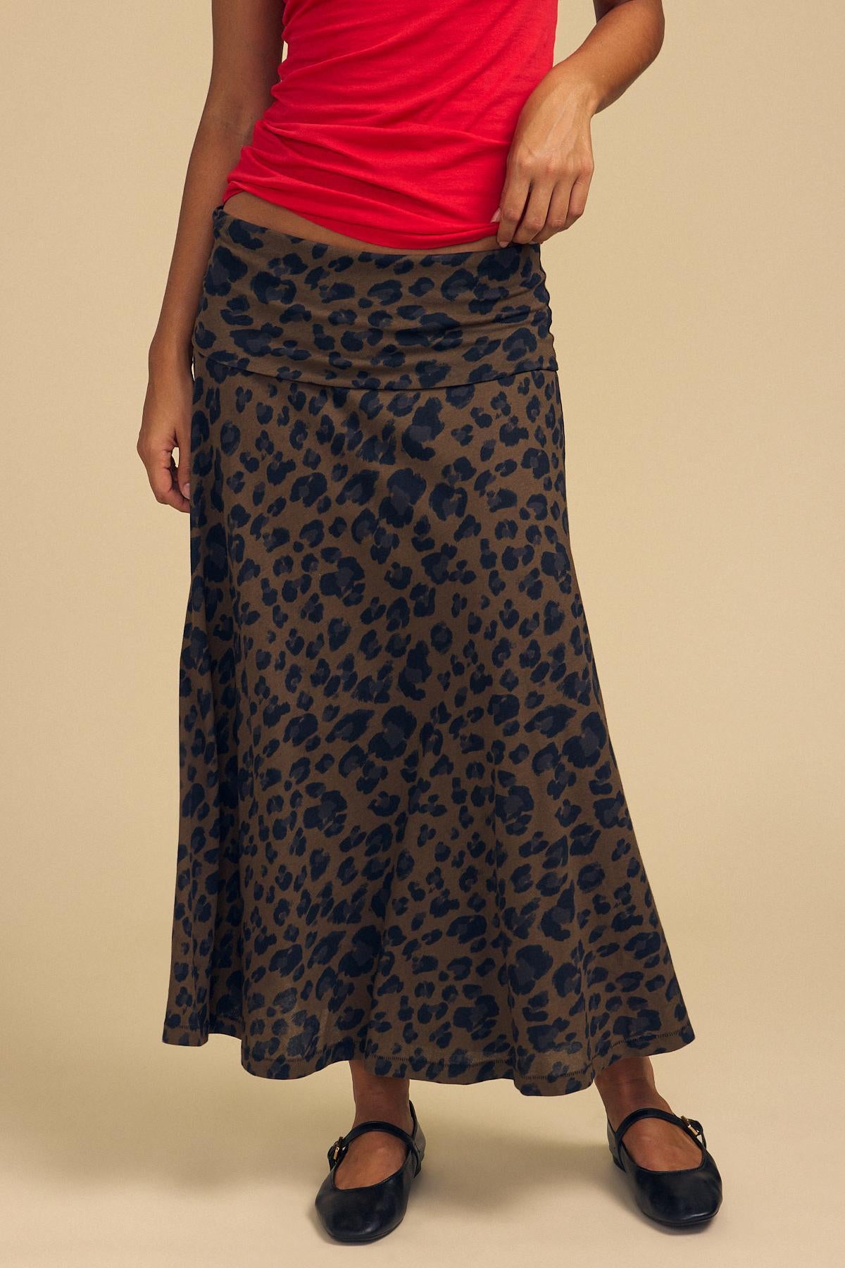 A person wearing a red sleeveless top, the VEDA SKIRT by Velvet by Graham & Spencer featuring a brown and black leopard print, and black ballet flats stands against a plain beige background.-42204643262657