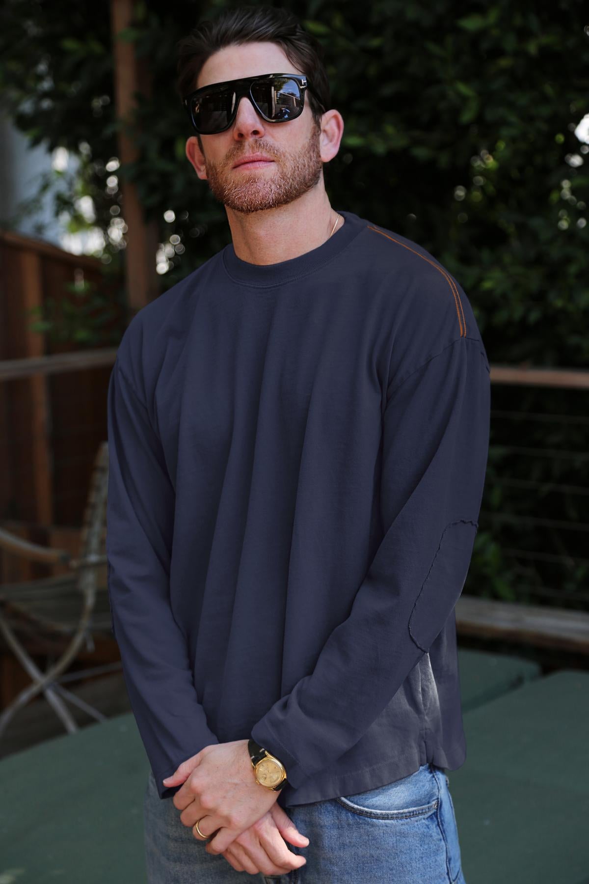   A man with a beard and sunglasses stands outdoors, sporting the SLATER TEE in a relaxed fit and structured pima cotton from Velvet by Graham & Spencer, along with a gold watch, adding versatility to his ensemble. 