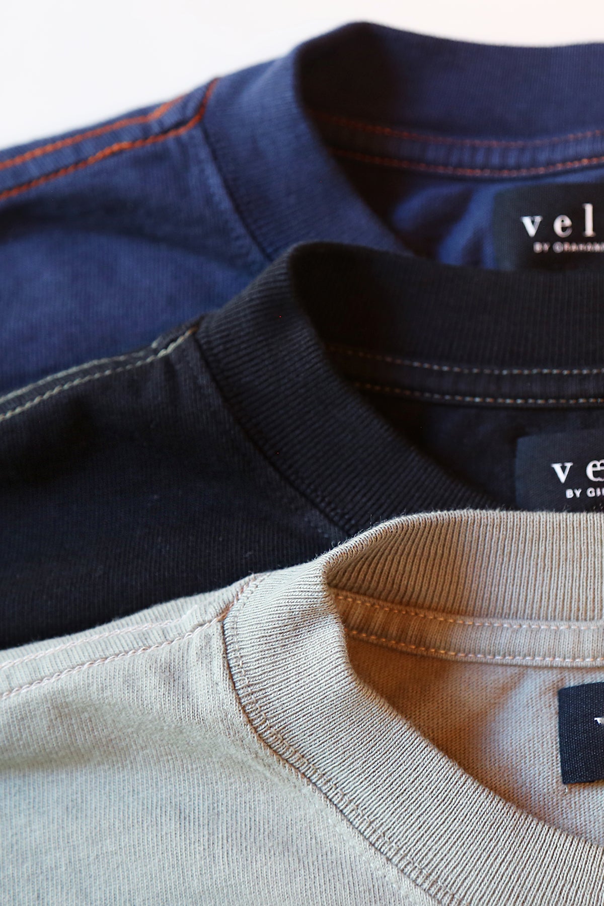   Three SLATER TEE crewneck shirts in navy, black, and beige, crafted from soft pima cotton jersey, arranged vertically. The tags displaying 'Velvet by Graham & Spencer' are visible. These relaxed fit essentials make a versatile wardrobe addition ideal for any occasion. 