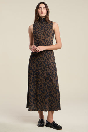 A woman stands wearing the KELESTINE DRESS by Velvet by Graham & Spencer, a sleeveless, ankle-length cotton jersey dress featuring a brown and black leopard print pattern, paired with black loafers.