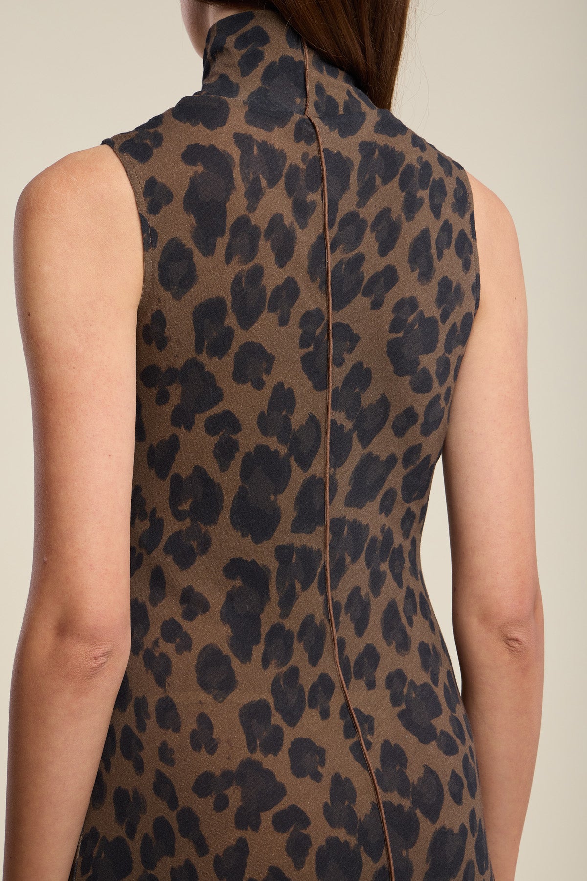 A woman is shown from the back wearing the KELESTINE DRESS by Velvet by Graham & Spencer—a sleeveless, high-neck dress featuring a brown and black leopard print with an elegant A-line skirt.-42063789129921