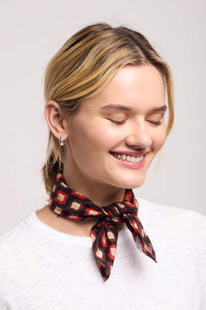 A woman with short blonde hair, in a white shirt and the JEWEL SCARF by Velvet by Graham & Spencer, smiles with her eyes closed against a plain background.