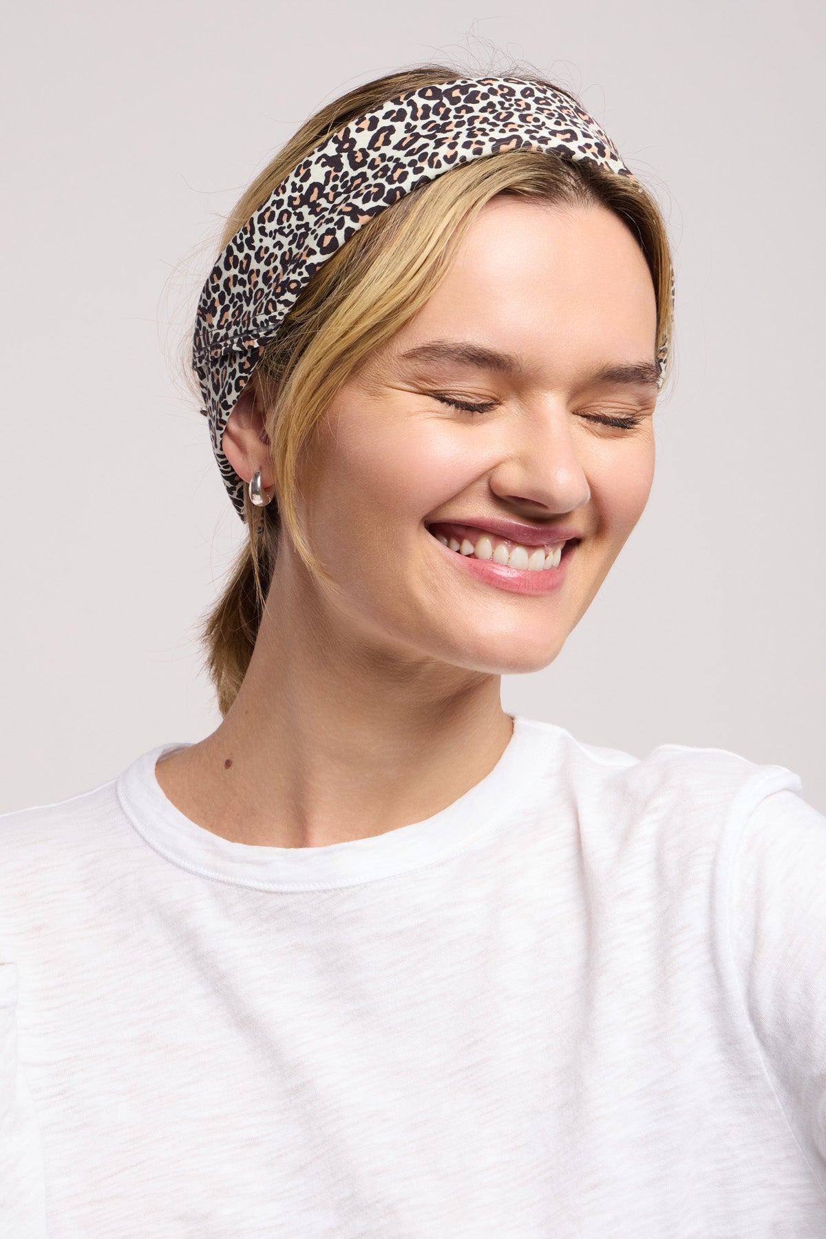 A person wears the JEWEL SCARF by Velvet by Graham & Spencer and a white shirt, smiling with eyes closed against a plain background.