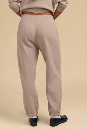 A person viewed from behind in a relaxed silhouette, wearing beige cotton fleece sweatpants with elasticized cuffs, paired with black loafers and a matching YOKO SWEATSHIRT by Velvet by Graham & Spencer.