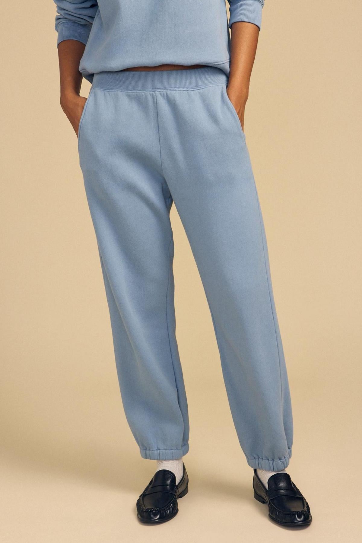 Person wearing relaxed fit, light blue ZARA SWEATPANT by Velvet by Graham & Spencer with matching sweatshirt, white socks, and black loafers, standing hands in pockets against beige backdrop.