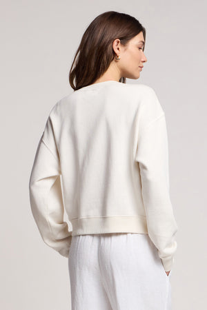 A person with long brown hair wears the off-white KENNA SWEATSHIRT by Velvet by Graham & Spencer and white pants, photographed from behind against a light background.
