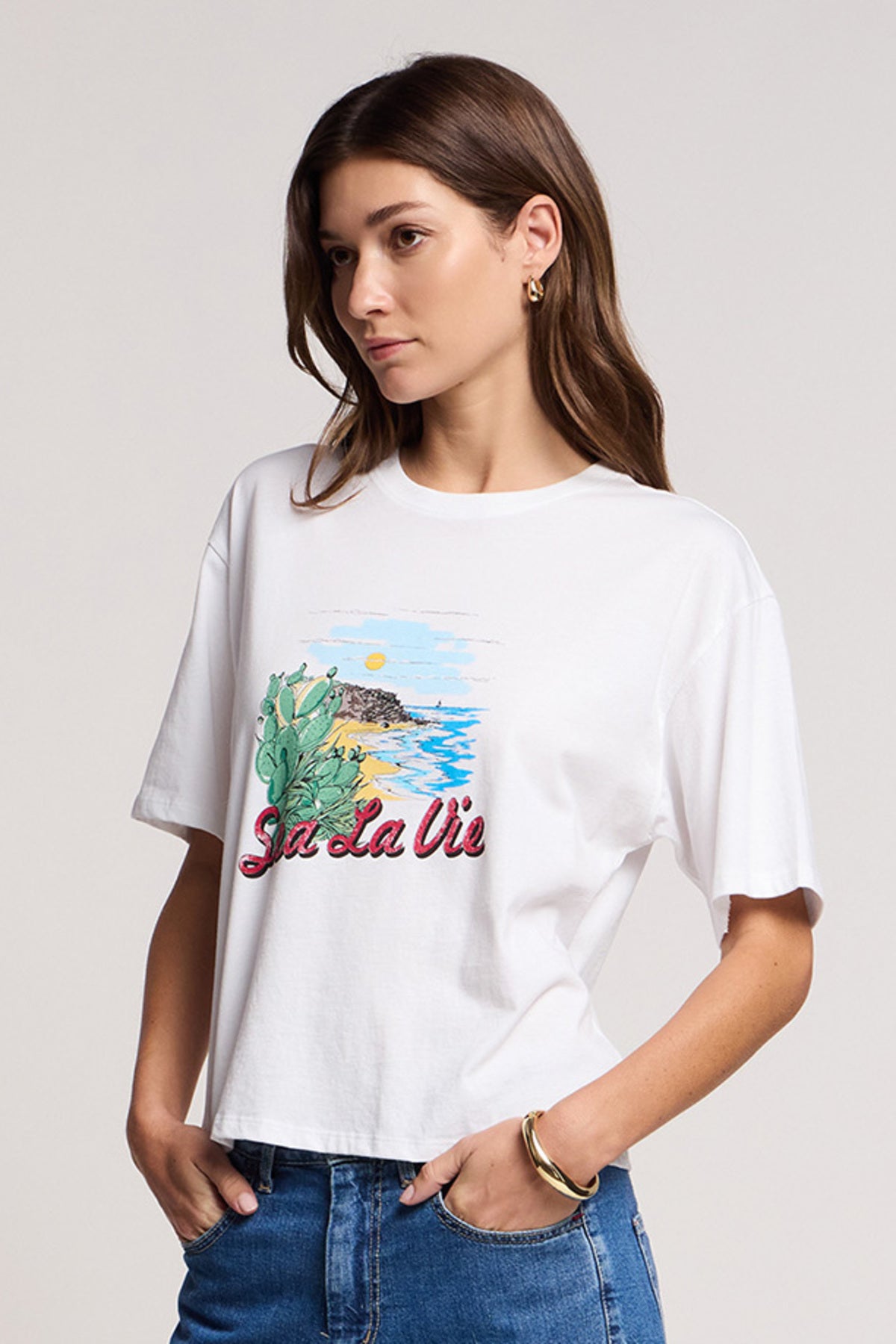 A woman wearing the SAMMY TEE by Velvet by Graham & Spencer—a relaxed white cotton jersey swing tee with a coastal scene and 