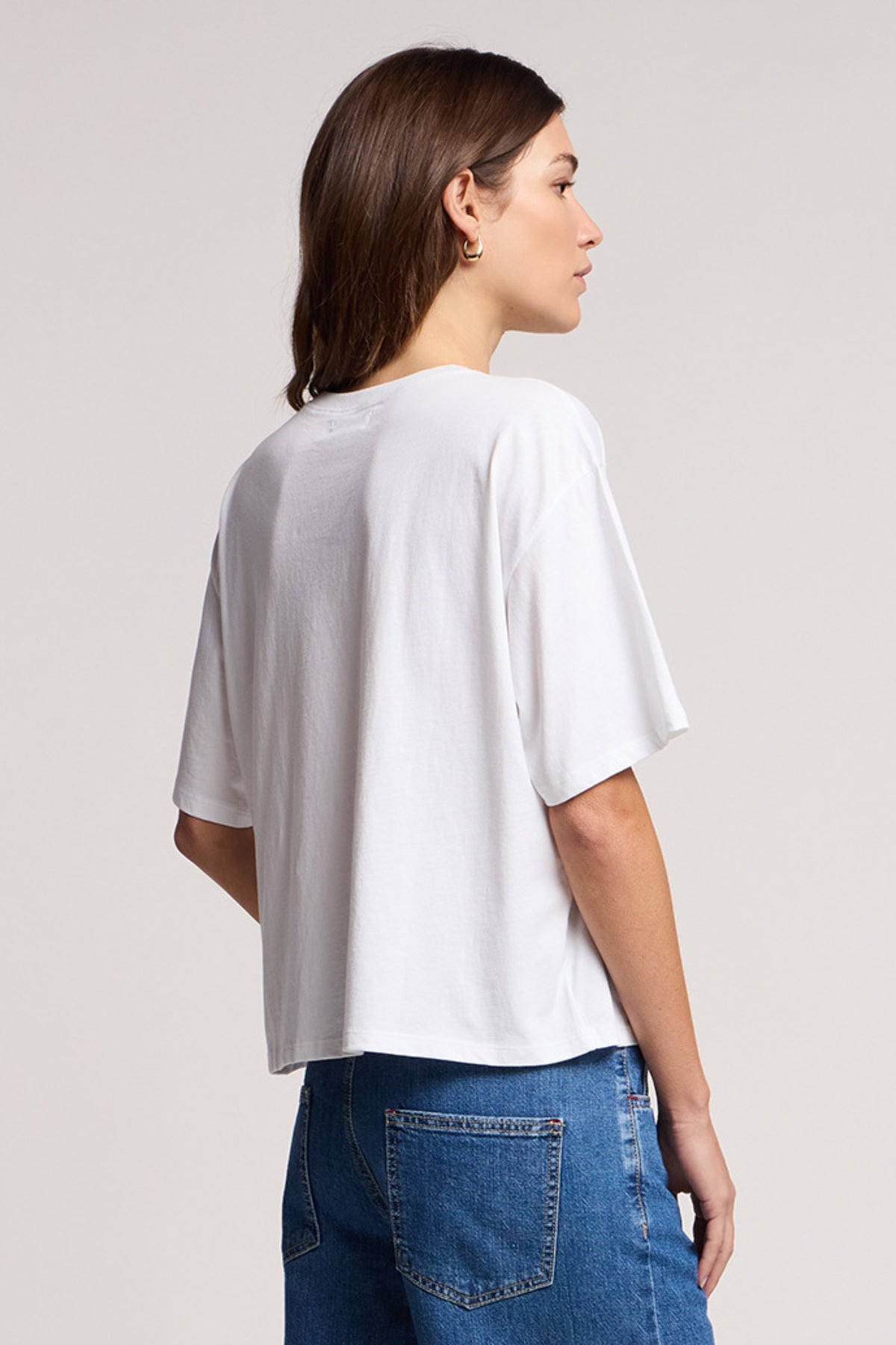 Someone faces away in the Velvet by Graham & Spencer SAMMY TEE, a relaxed swing top in plain white, paired with blue jeans against a neutral background.-41374555013313