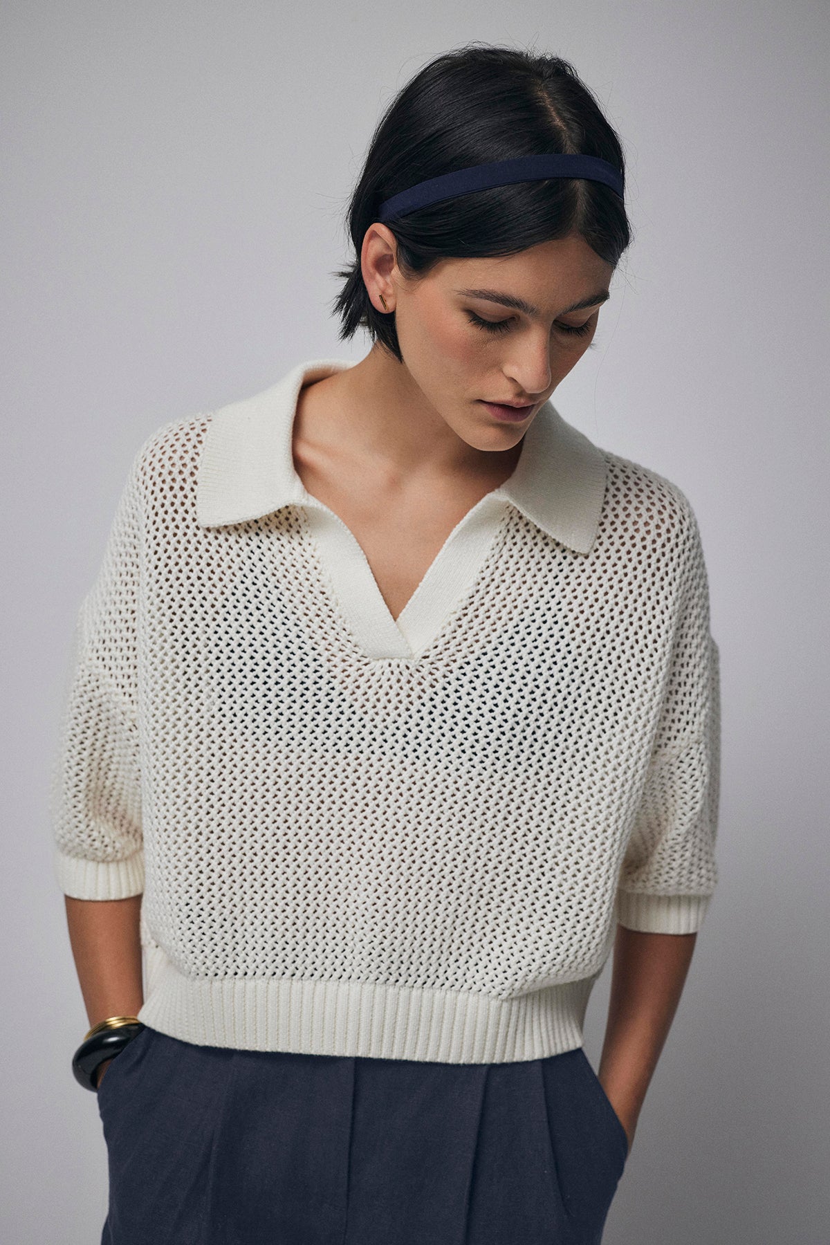   A person wearing a white YORK SWEATER POLO by Velvet by Jenny Graham and dark pants looks down with a neutral expression, exuding casual charm. 