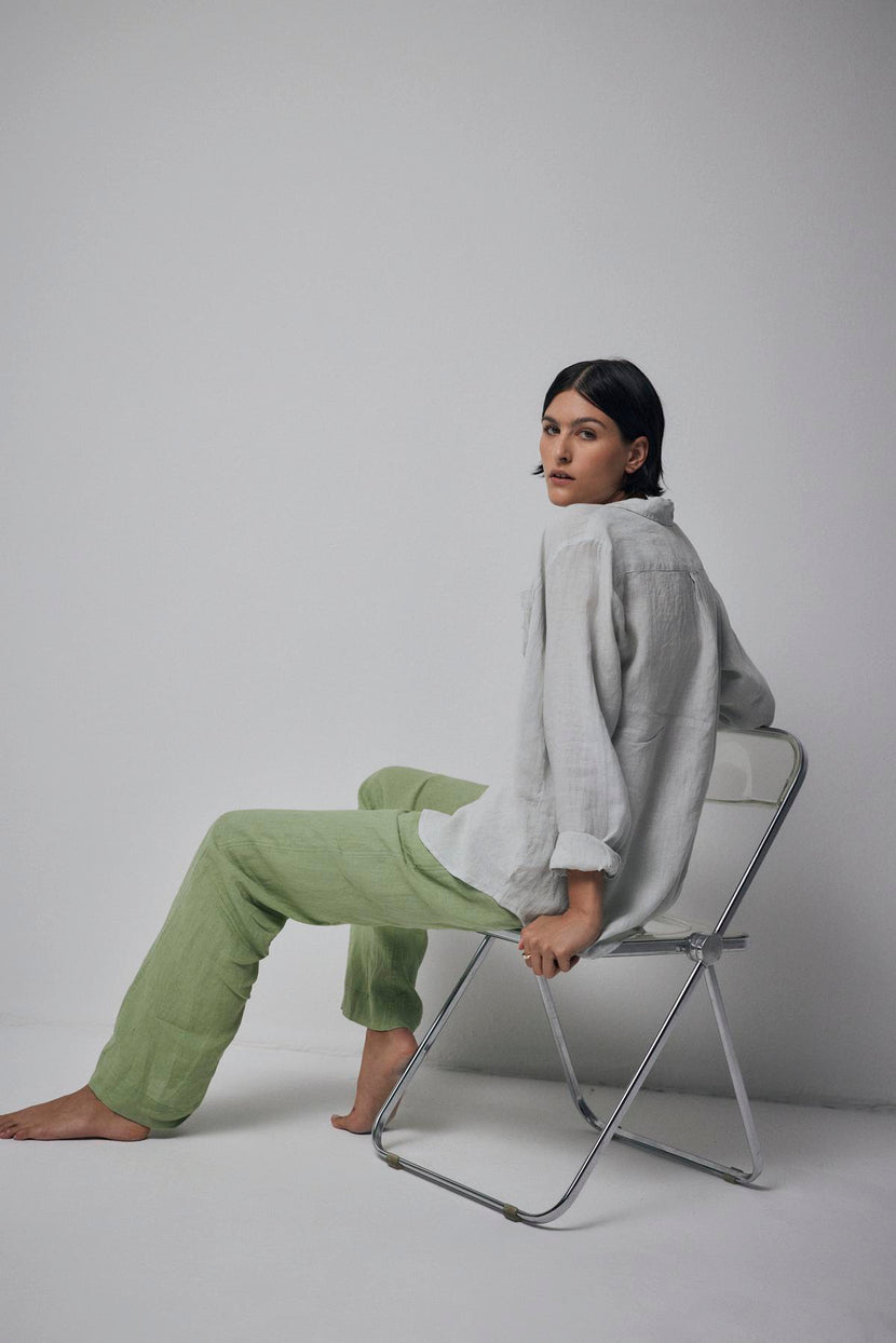 A woman sitting on a chair in green linen pants with a relaxed silhouette by Velvet by Jenny Graham.
