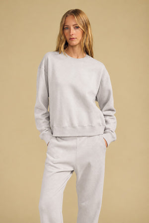 A woman wearing a relaxed YOKO SWEATSHIRT and matching sweatpants with her hands in her pockets.