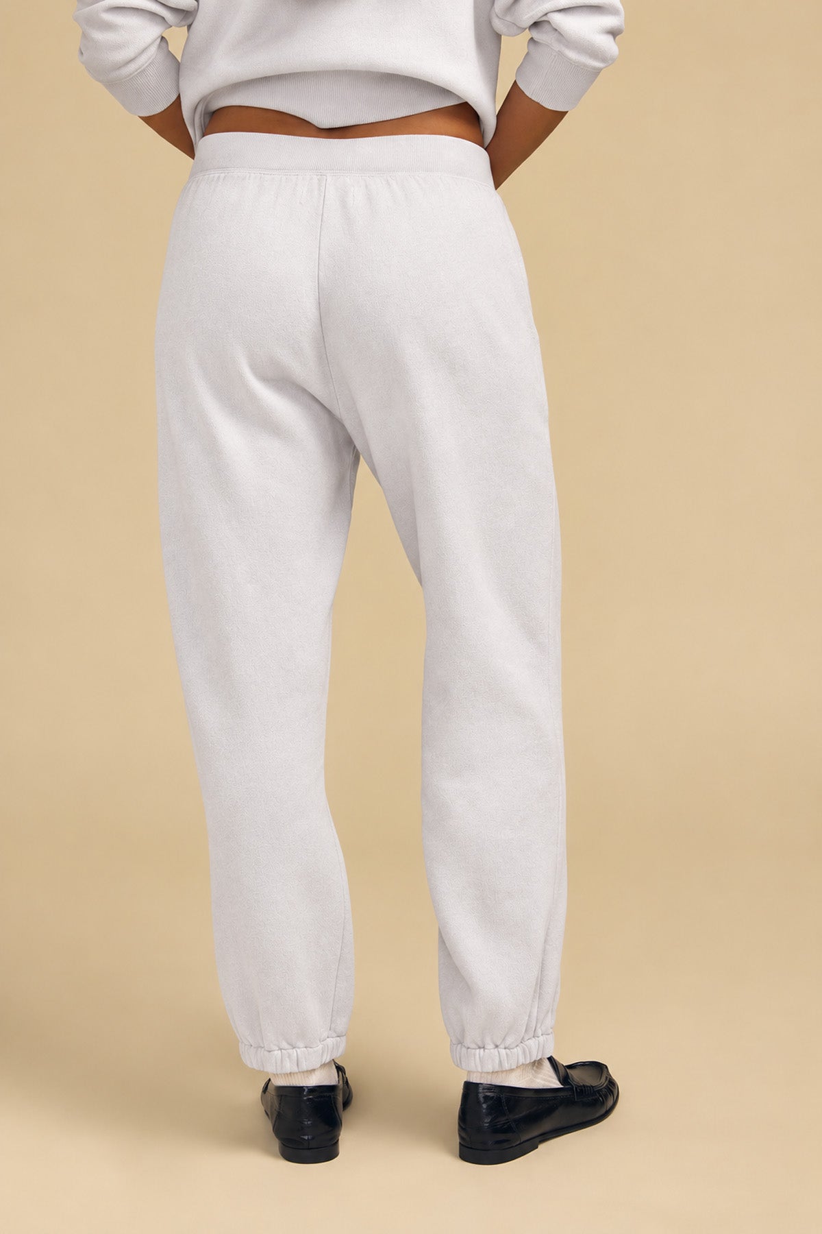 Back view of a person wearing light gray cotton fleece sweatpants with elastic cuffs and a matching relaxed YOKO SWEATSHIRT, paired with black loafers.-46320580493505