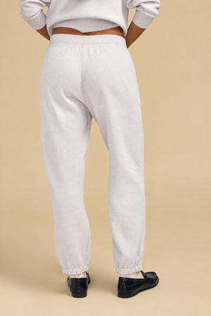 Back view of a person wearing light gray cotton fleece sweatpants with elastic cuffs and a matching relaxed YOKO SWEATSHIRT, paired with black loafers.