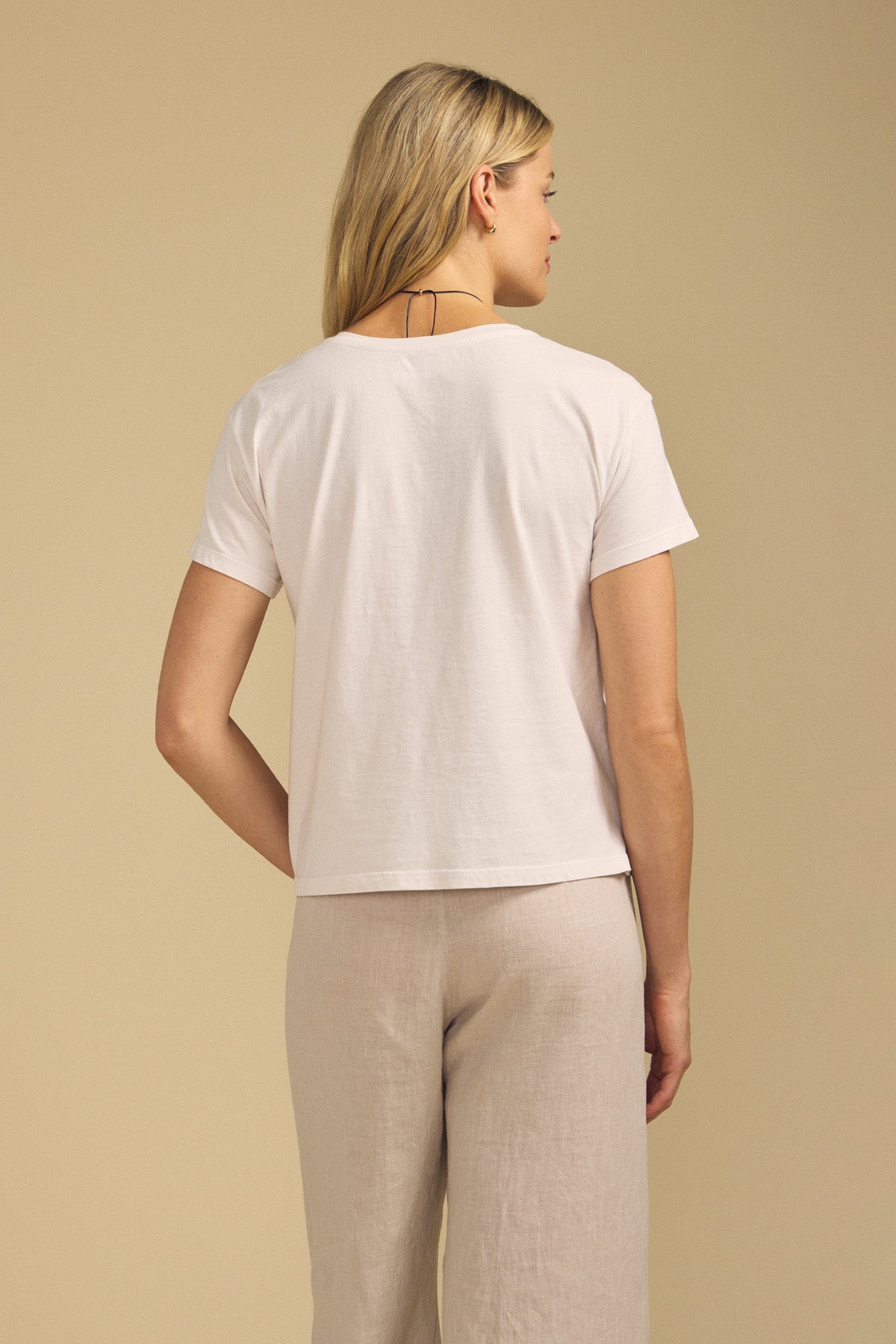 Back view of TIA cotton jersey short-sleeve crew-neck tee showcasing white cotton jersey with beige pants against a beige background