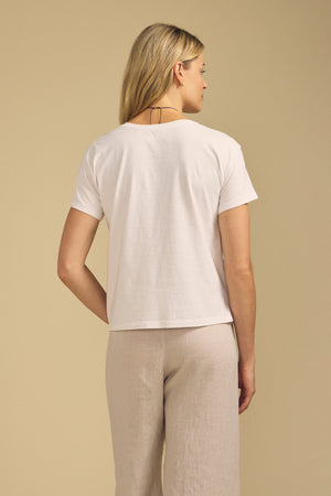 Back view of TIA cotton jersey short-sleeve crew-neck tee showcasing white cotton jersey with beige pants against a beige background