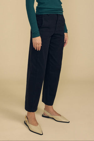 A person wearing a green long-sleeve top, the TENLEY PANT by Velvet by Graham & Spencer in black high-waisted wide-leg style, and beige pointed flats stands against a plain beige background.