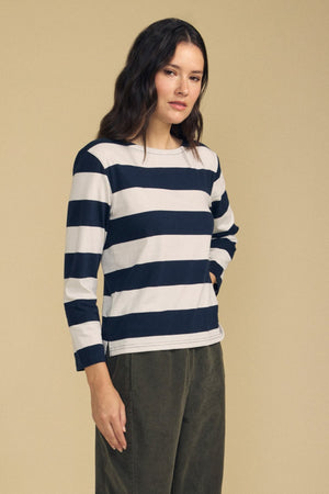 A woman stands against a beige background wearing the GABRIELA TEE by Velvet by Graham & Spencer, a relaxed fit, long sleeve striped cotton jersey top in black and white, paired with olive green pants.