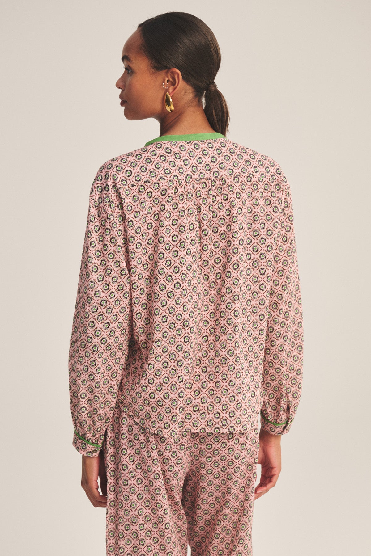 A person with pulled-back hair is seen from the back, wearing the KARMEN TOP by Velvet by Graham & Spencer and matching pants in a pink and green geometric pattern.-41088948240577
