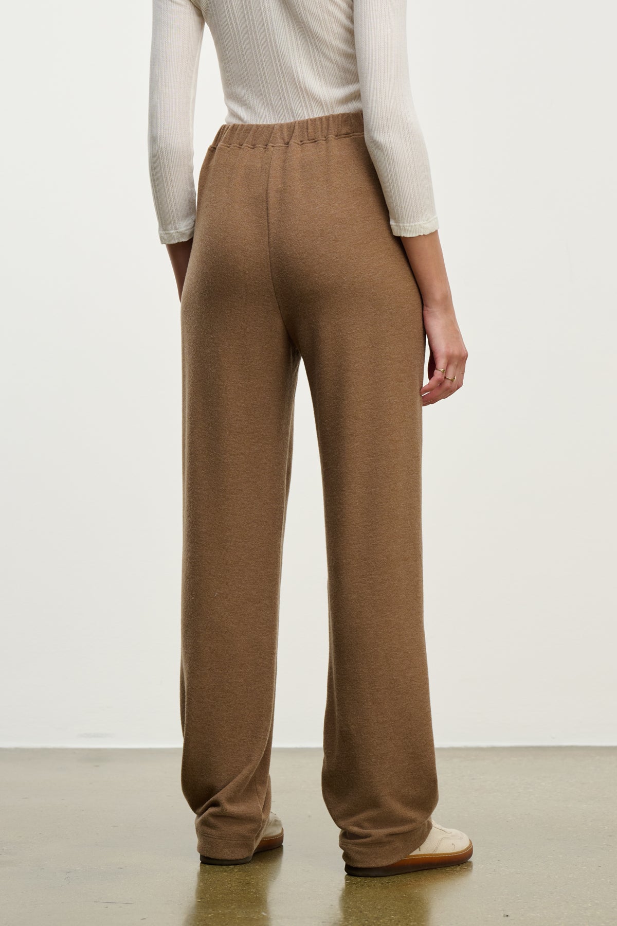 Someone stands on a light brown floor, facing away from the camera, wearing the ELIYA SWEATPANT by Velvet by Graham & Spencer and a white ribbed long-sleeve top.-39838349394113