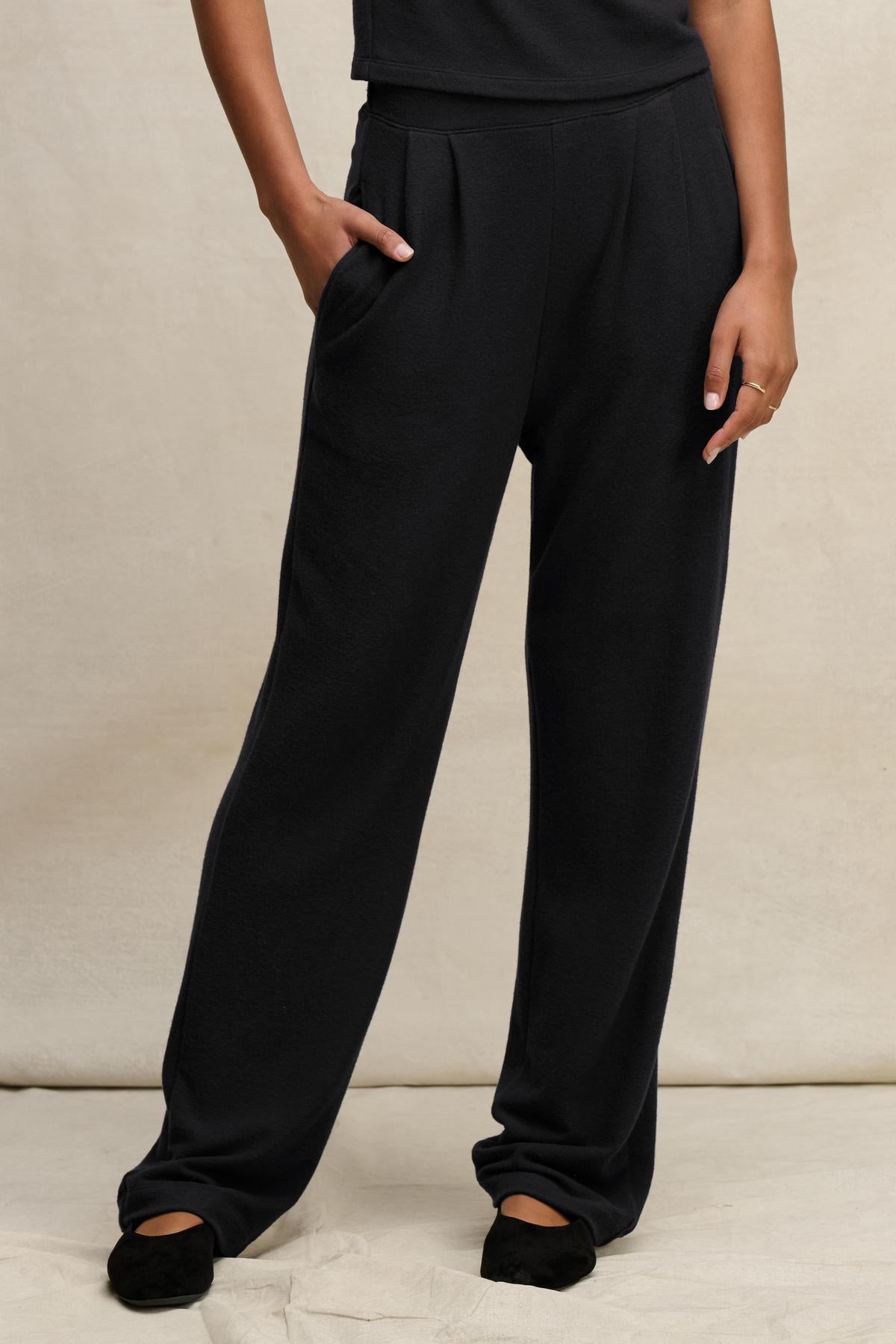 Wearing the ELIYA SWEATPANT by Velvet by Graham & Spencer, someone stands with one hand in their pocket, paired with a black top and shoes, against a neutral background.-40481741111489