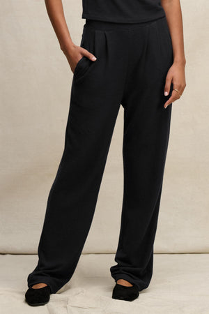 Wearing the ELIYA SWEATPANT by Velvet by Graham & Spencer, someone stands with one hand in their pocket, paired with a black top and shoes, against a neutral background.