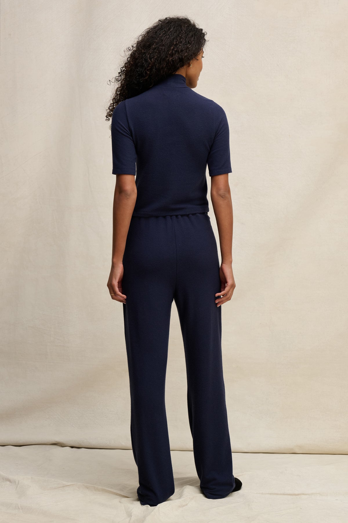 A person with curly hair faces away, wearing Velvet by Graham & Spencer's ELIYA SWEATPANT and a navy short-sleeve top, showcasing the ultra-soft, comfortable fit against a neutral background.-39838349164737