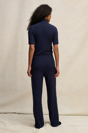 A person with curly hair faces away, wearing Velvet by Graham & Spencer's ELIYA SWEATPANT and a navy short-sleeve top, showcasing the ultra-soft, comfortable fit against a neutral background.