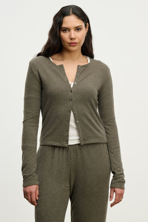 A woman models the RAYA CARDIGAN by Velvet by Graham & Spencer in olive green, paired with matching pants and a white ribbed top, standing against a plain light background.