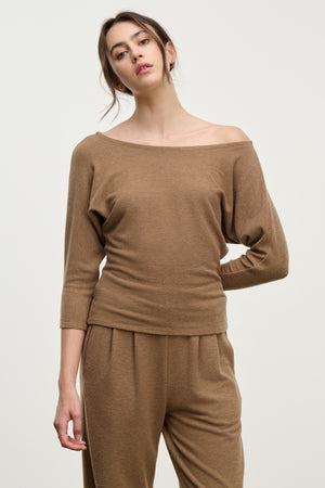 A woman wears the SELENA TOP by Velvet by Graham & Spencer—a relaxed, brown boatneck—paired with matching pants, standing against a plain light background.