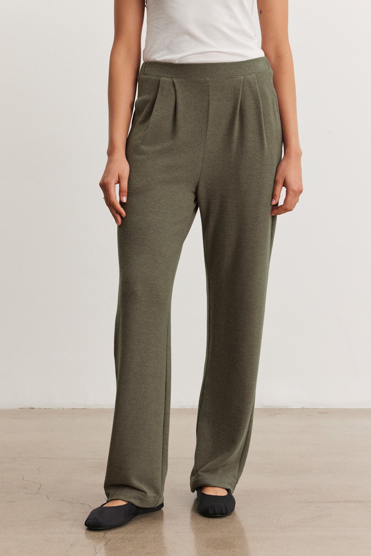 A person wearing Velvet by Graham & Spencer's ELIYA SWEATPANT in olive green with a wide-leg fit and a white top stands on a polished floor, shown from the waist down.