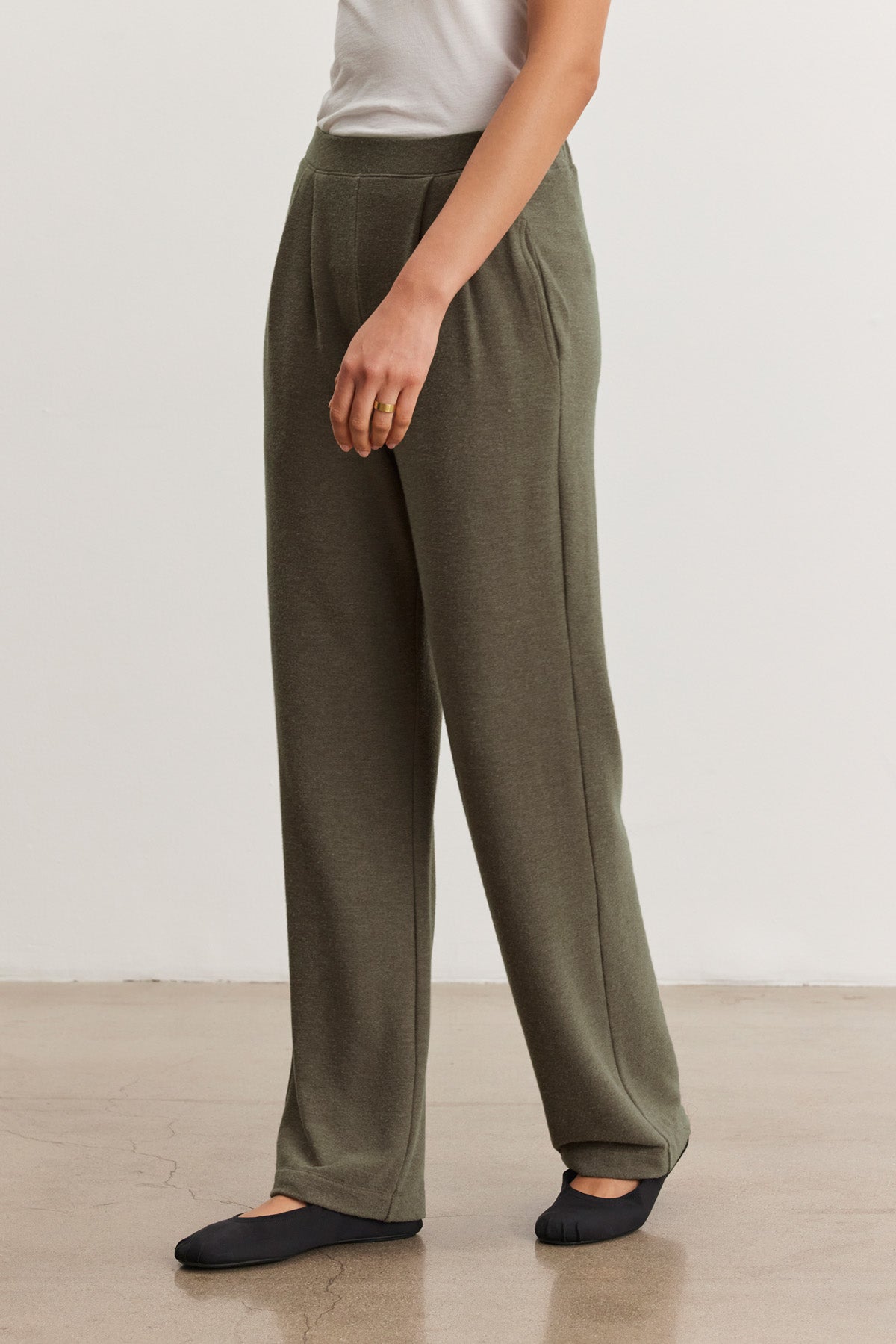 A person stands indoors wearing Velvet by Graham & Spencer's ELIYA SWEATPANT in olive green, paired with a white top and black flats, hands relaxed at their sides.-40499990102209