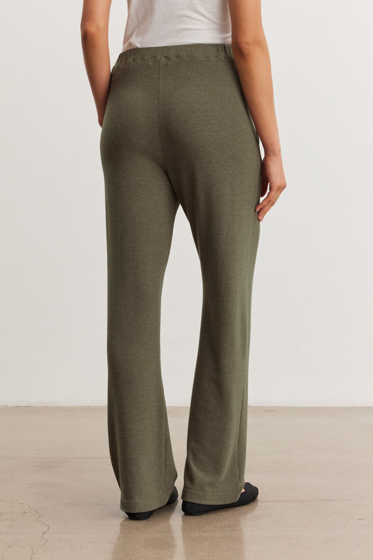 A person, shown from the back, stands on a polished floor wearing the ELIYA SWEATPANT in olive green by Velvet by Graham & Spencer and a white top.