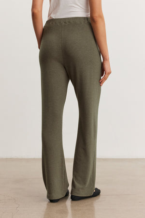 A person, shown from the back, stands on a polished floor wearing the ELIYA SWEATPANT in olive green by Velvet by Graham & Spencer and a white top.