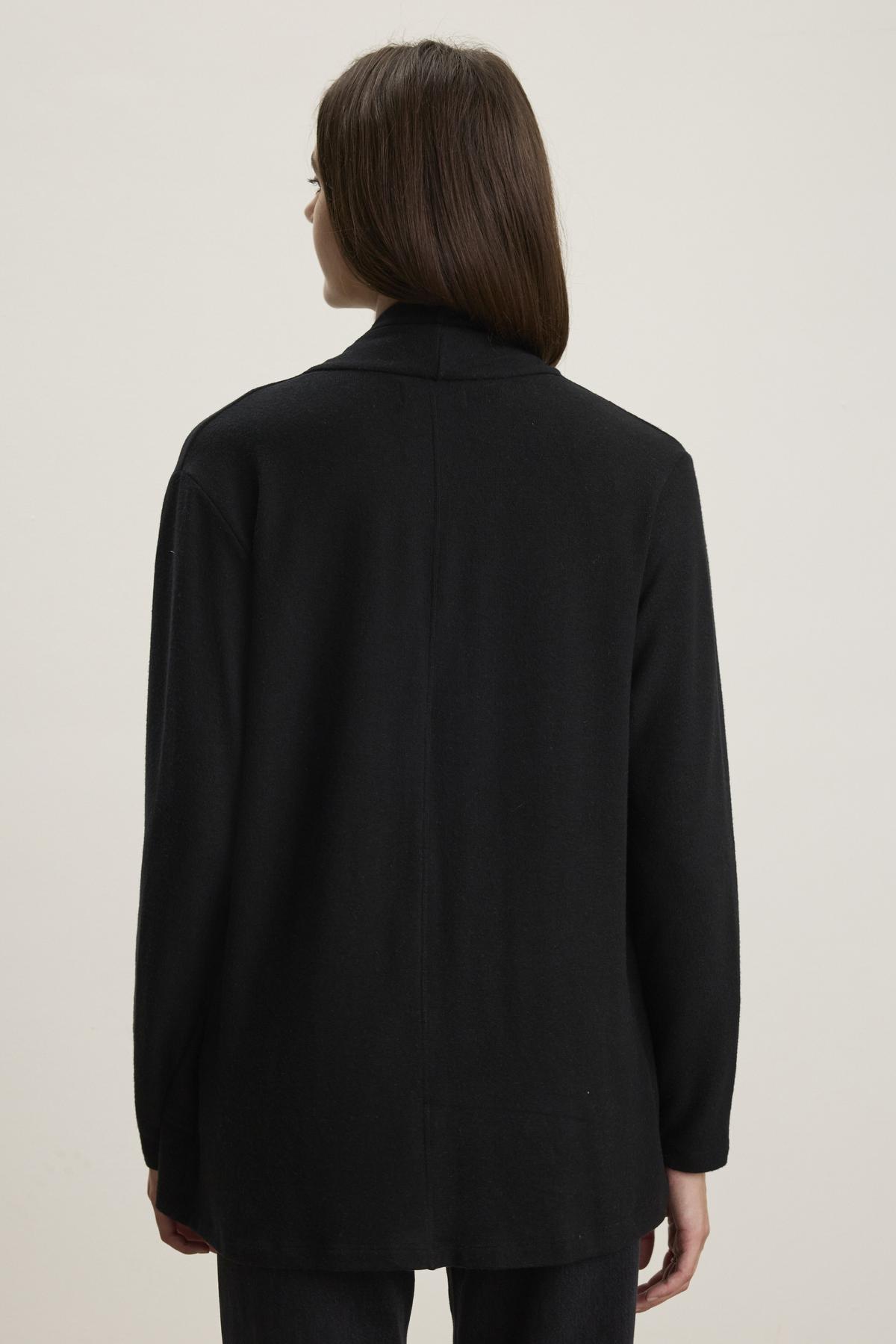   A person with long dark hair is pictured from behind against a plain background, wearing the LISA CARDIGAN by Velvet by Graham & Spencer, featuring an open front and side patch pockets in black triblend knit. 