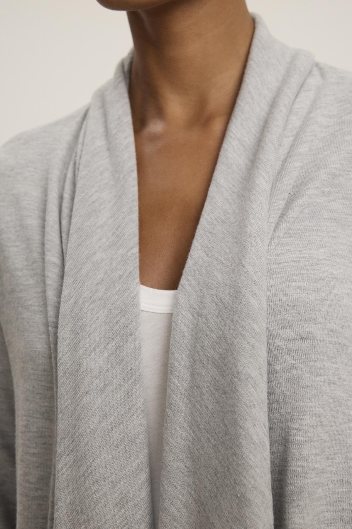   Close-up of a person wearing the LISA CARDIGAN from Velvet by Graham & Spencer over a white top. The luxurious triblend knit showcases an open front, with a soft, loose collar and side patch pockets. 