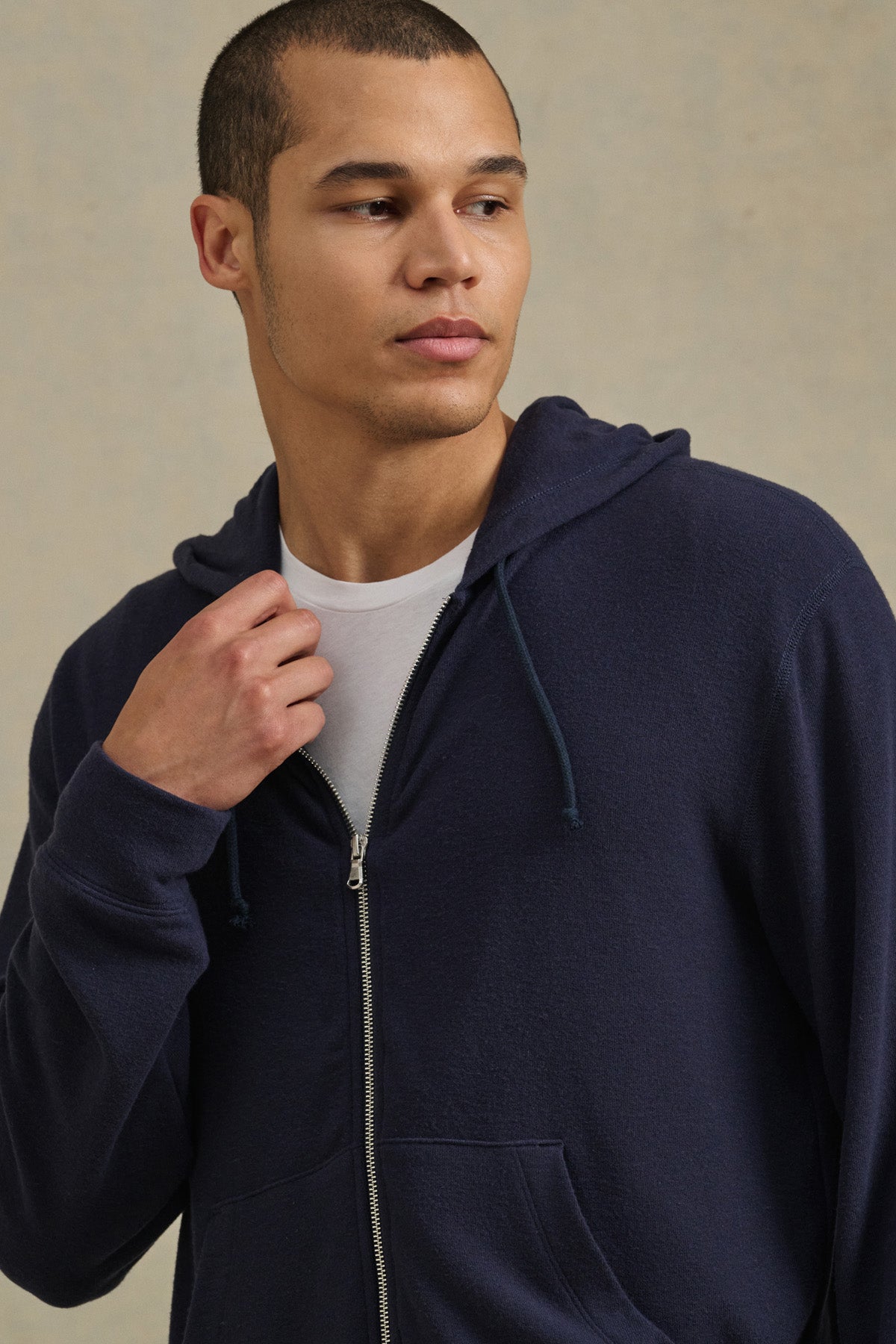 A person models the PORTER HOODIE by Velvet by Graham & Spencer, styled in navy blue over a white tee, looking to the side against a plain background for an effortlessly casual look.