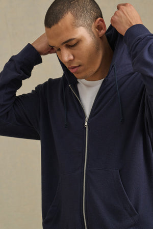 Wearing the PORTER HOODIE by Velvet by Graham & Spencer over a white tee, a person adjusts the hood, highlighting relaxed casual style.