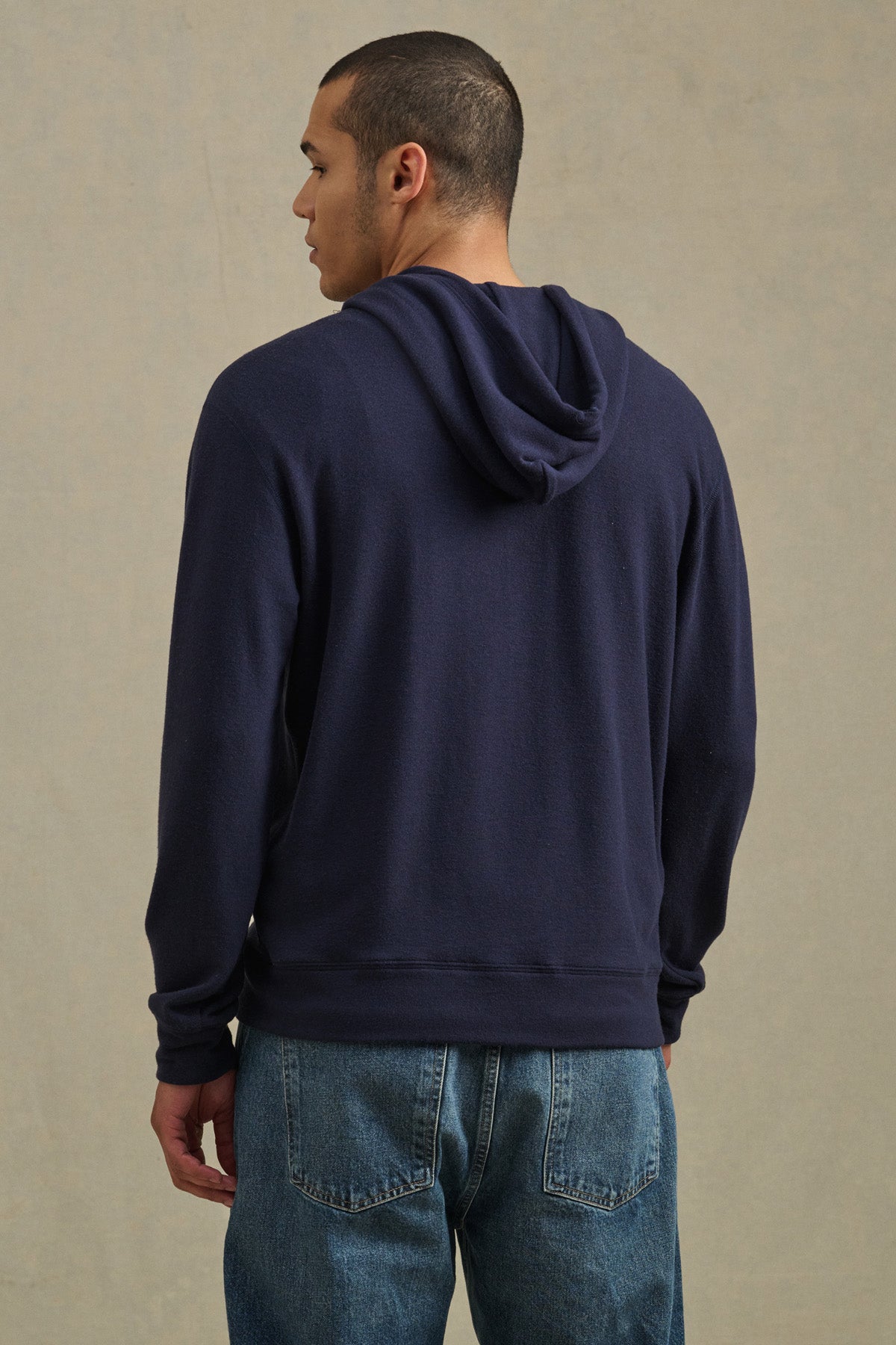 Wearing the Velvet by Graham & Spencer PORTER HOODIE in navy blue and blue jeans, a person stands with their back to the camera, highlighting a relaxed casual look against a neutral background.-41009056612545