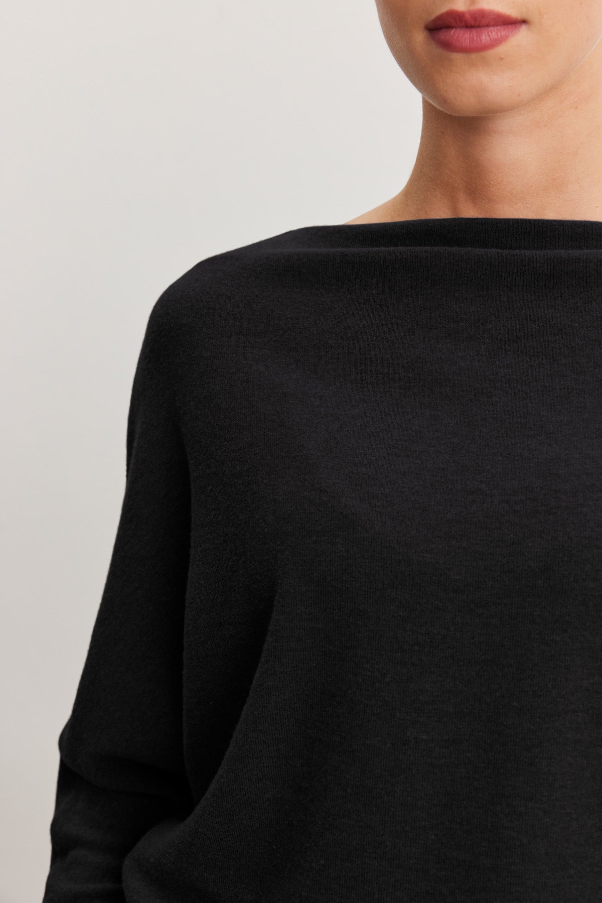 A woman is shown from the shoulders to the lips wearing the SELMY TOP, a black triblend knit long-sleeve boat neck by Velvet by Graham & Spencer, against a plain background.