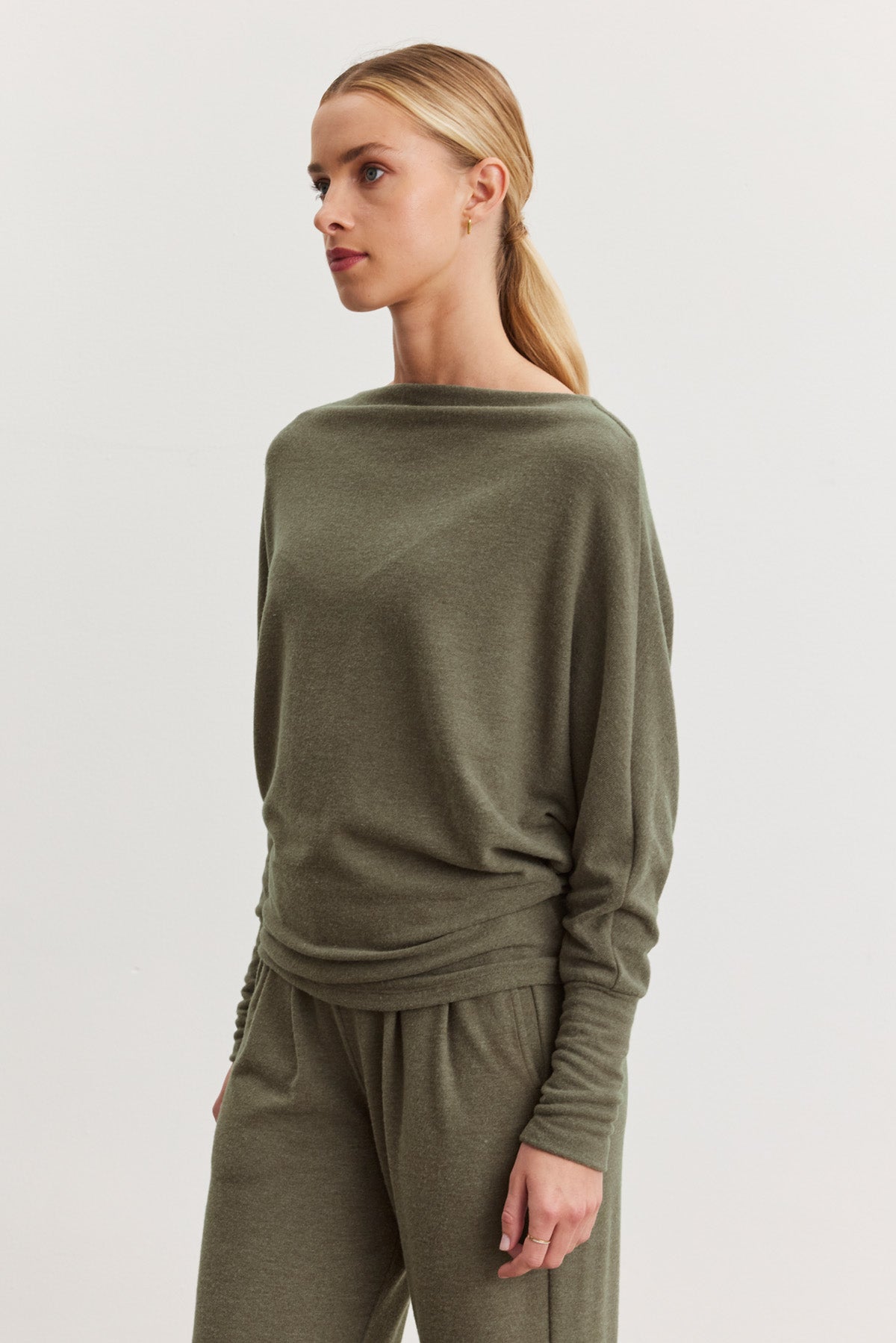 A woman with blonde hair in a low ponytail wears the SELMY TOP by Velvet by Graham & Spencer in olive green, paired with matching pants, and stands against a plain light background.-40500009304257