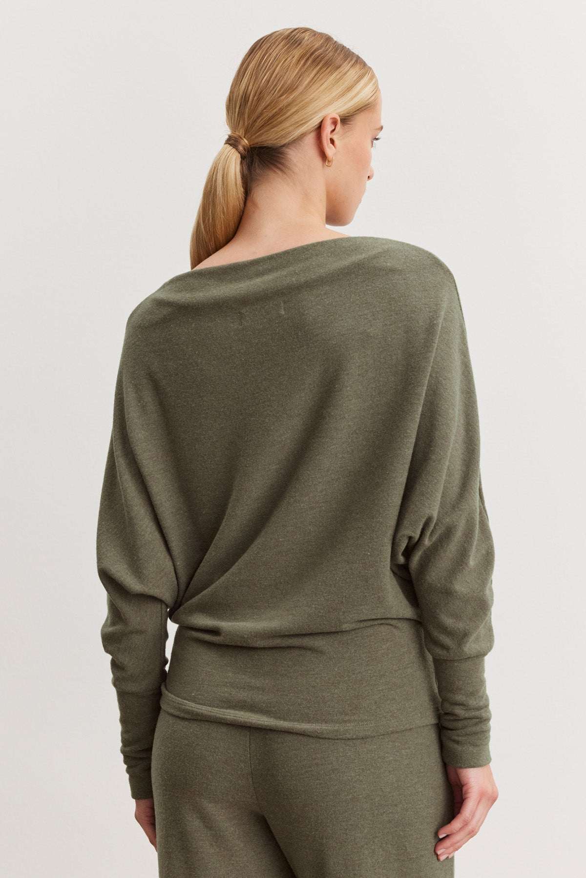 A woman with blonde hair in a low ponytail is seen from the back, wearing the SELMY TOP by Velvet by Graham & Spencer in olive green triblend knit, styled with matching pants.-40500009271489