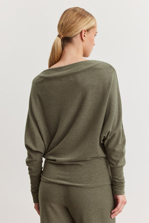 A woman with blonde hair in a low ponytail is seen from the back, wearing the SELMY TOP by Velvet by Graham & Spencer in olive green triblend knit, styled with matching pants.
