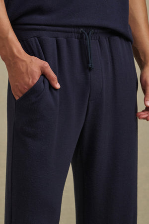 Model wears the EASTON SWEATPANT by Velvet by Graham & Spencer in navy blue, made from a soft tri-blend fabric, with one hand in the elastic waist pocket, shown from waist to mid-thigh.