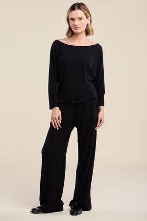Wearing the CECILIA TOP by Velvet by Graham & Spencer, styled with black wide-leg pants, the person stands against a plain beige background.