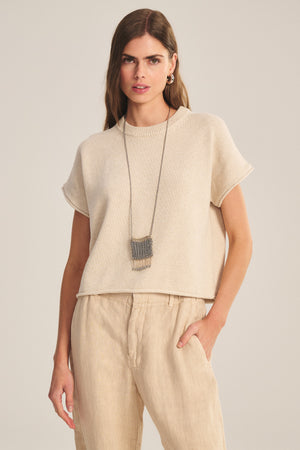 A woman wears the KEENY SWEATER by Velvet by Graham & Spencer, styled with light pants and a long pendant necklace, standing against a neutral background.