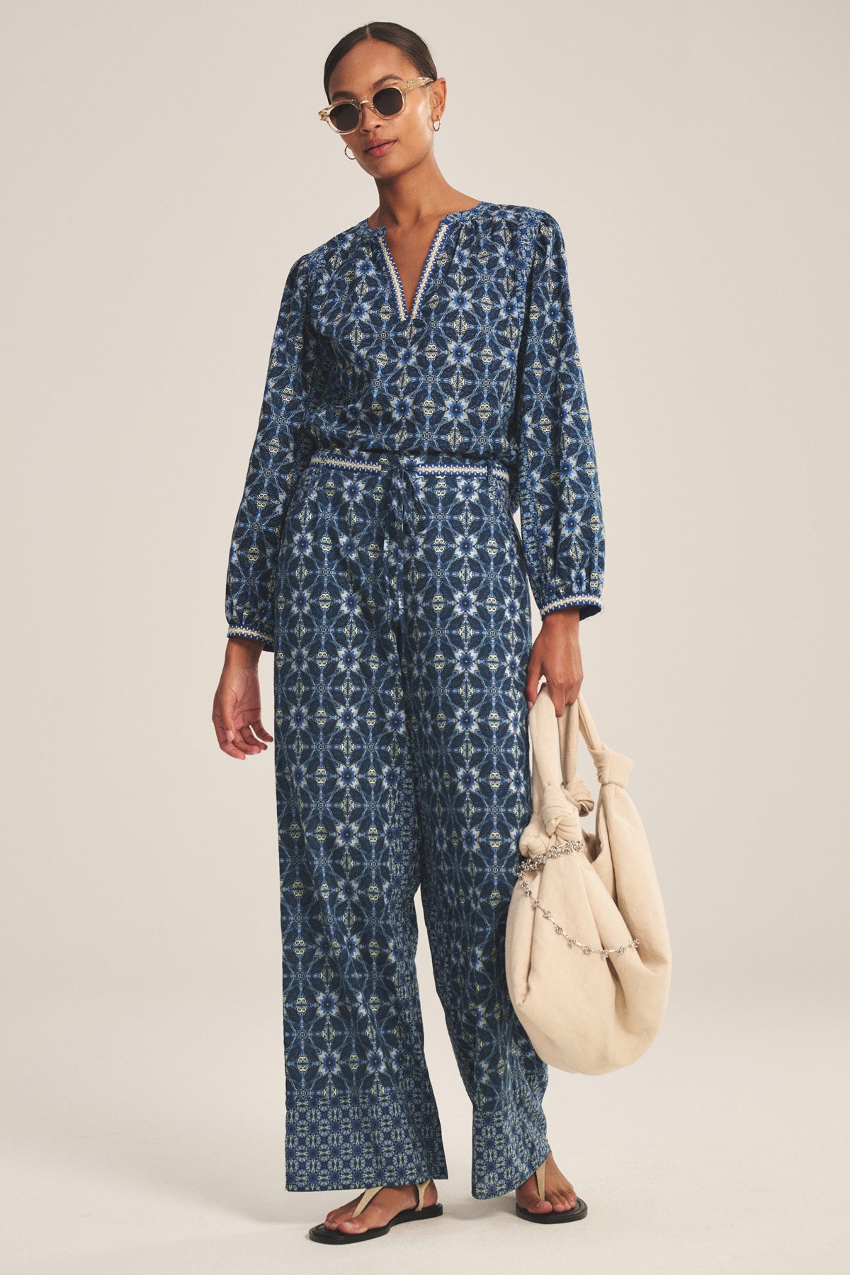 A woman wears the CLAUDIE TOP by Velvet by Graham & Spencer, styled with sunglasses and a large beige bag, standing against a plain background.