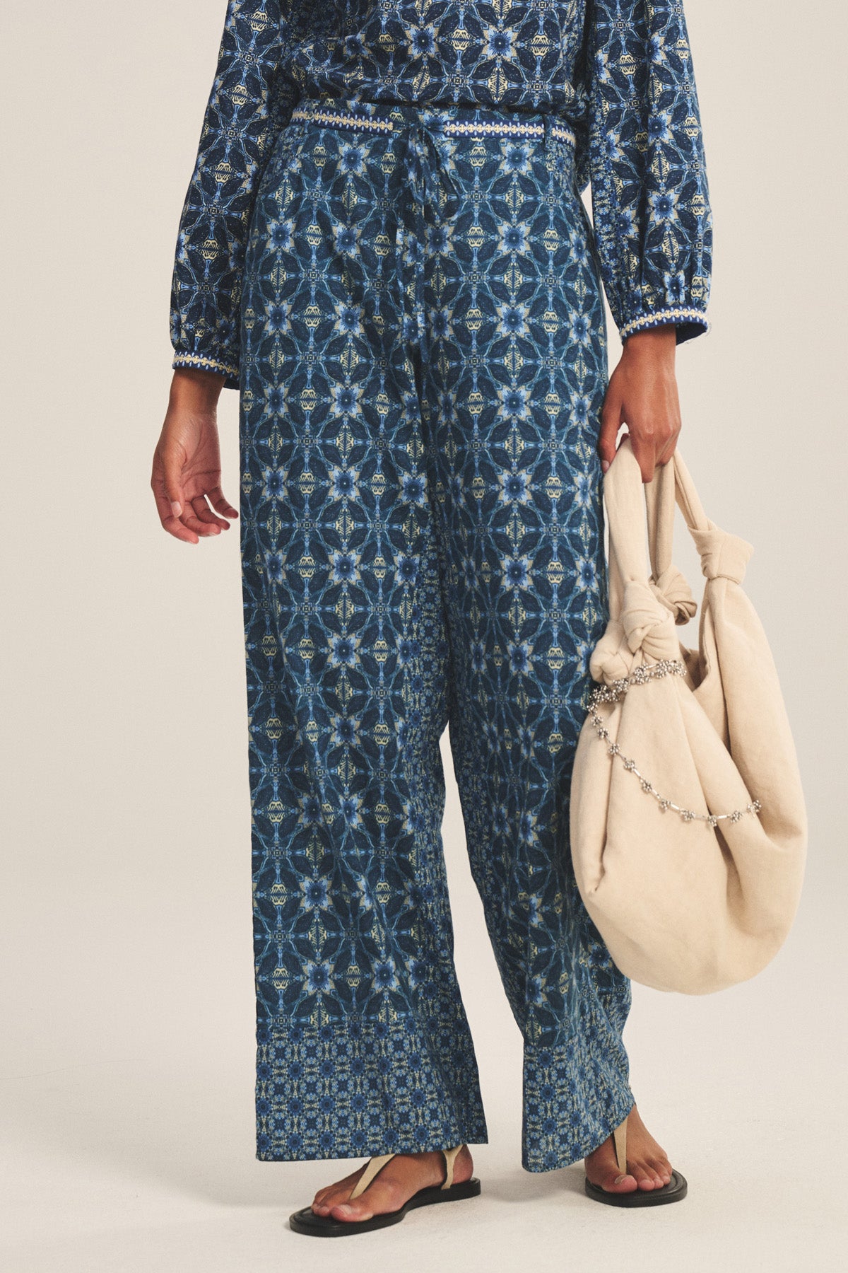 A person wears the KENDRA PANT by Velvet by Graham & Spencer with a matching top, carries a beige bag with a chain detail, and wears black sandals.