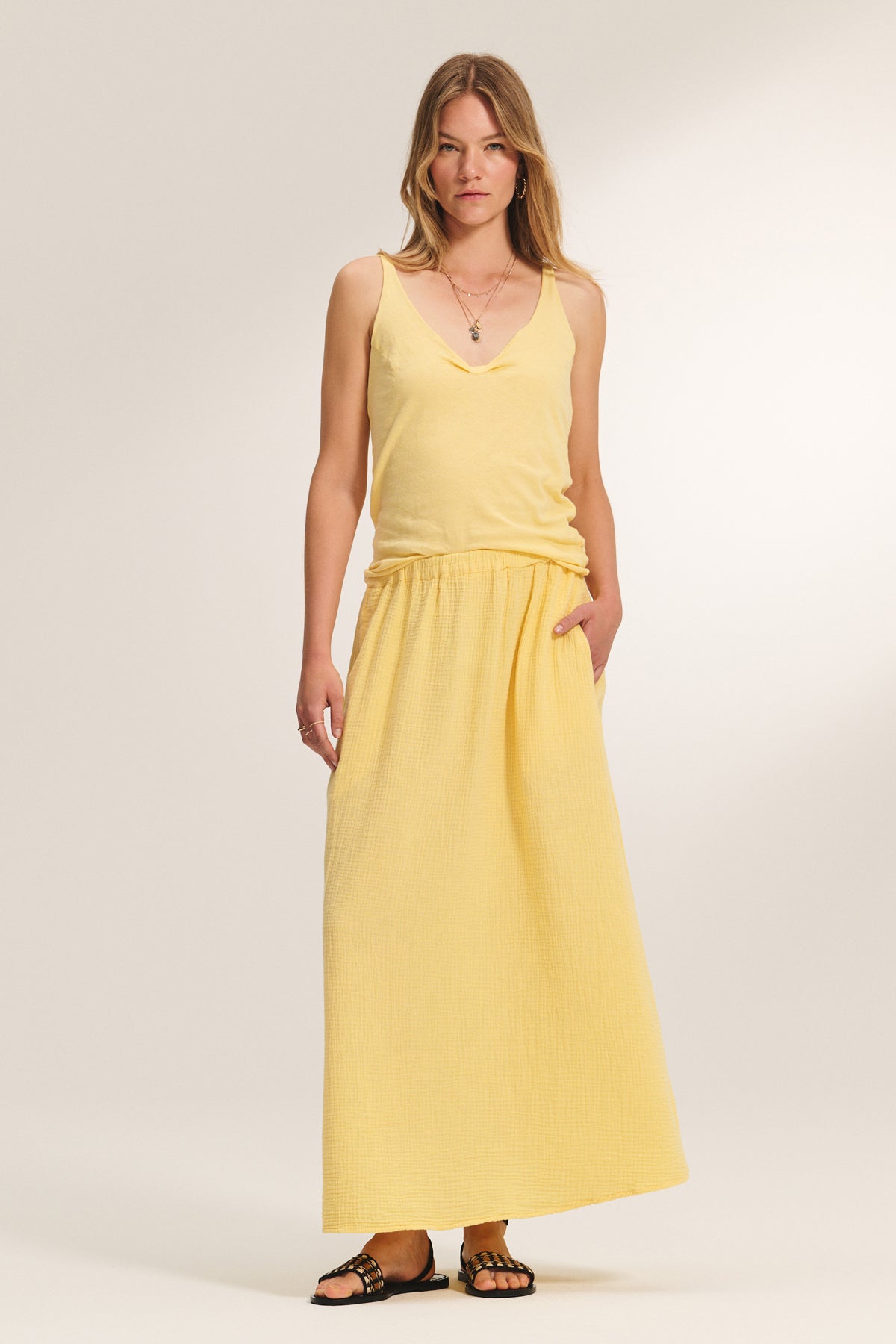 A woman stands facing forward wearing the KIM TANK TOP by Velvet by Graham & Spencer, a lightweight cotton tank with a scoop neckline, paired with a matching long yellow skirt and black sandals against a plain light background.-39173077762241