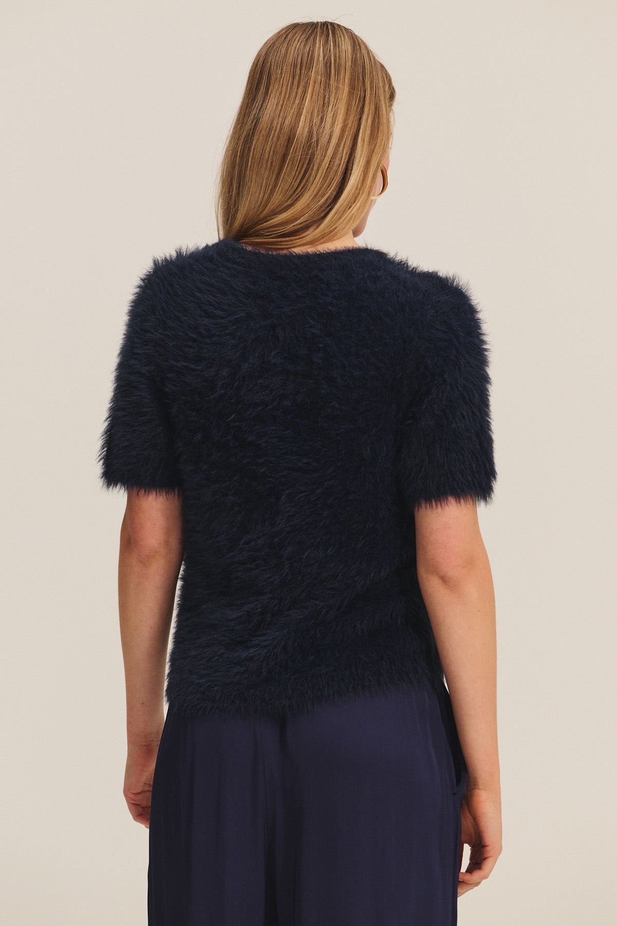 A woman with long, light brown hair is shown from the back, wearing Velvet by Graham & Spencer's KIT SWEATER and matching navy skirt for lightweight comfort.