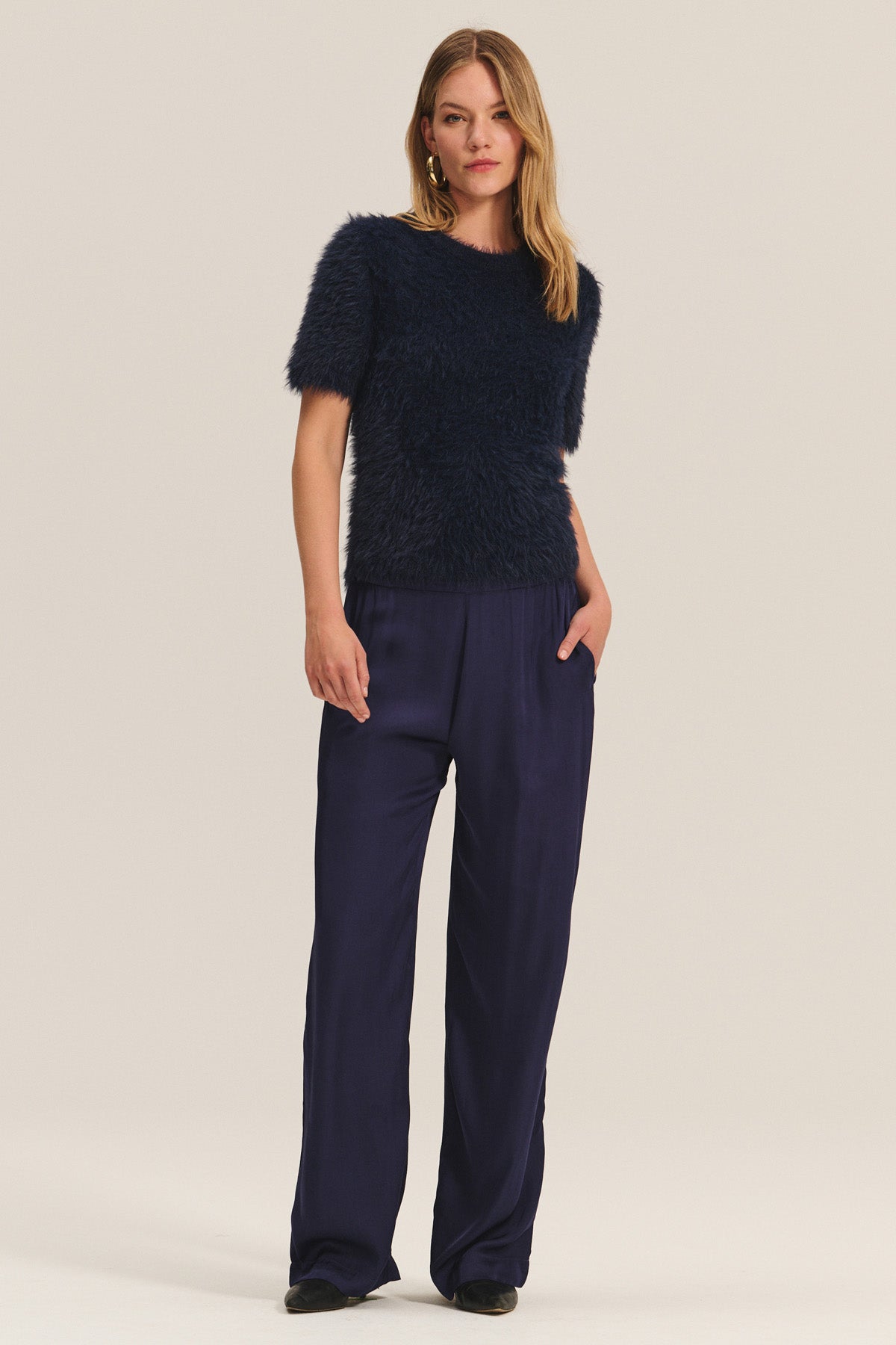   A woman poses against a plain background wearing the LARKIN PANT from Velvet by Graham & Spencer, styled with one hand in her pocket for a relaxed, flattering look that's ideal for everyday wear. 